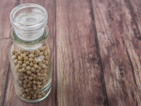 White peppercorn in glass vial over wooden background
