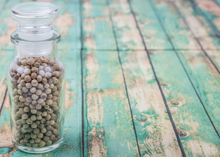 White peppercorn in glass vial over wooden background