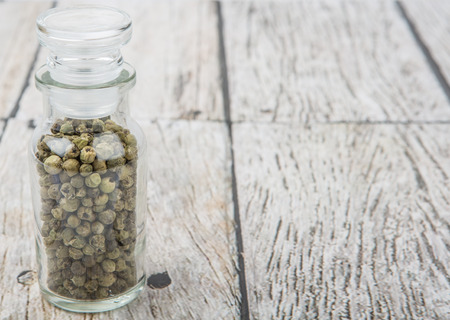 Green peppercorn in glass vial over wooden background