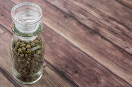 Green peppercorn in glass vial over wooden backgroundの写真素材