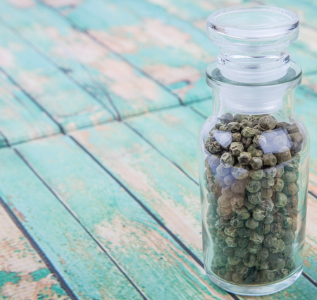 Green peppercorn in glass vial over wooden backgroundの写真素材