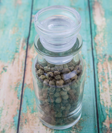 Green peppercorn in glass vial over wooden backgroundの写真素材