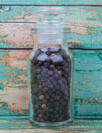 Black peppercorn in glass vial over wooden background