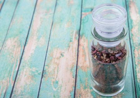 Sichuan pepper or peppercorn also known as Chinese coriander in glass vial over wooden backgroundの写真素材