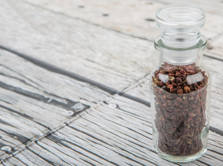 Sichuan pepper or peppercorn also known as Chinese coriander in glass vial over wooden backgroundの写真素材