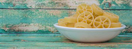 Dried wagon wheel shape pasta or rotelle pasta in white bowl over wooden backgroundの写真素材