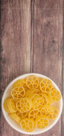 Dried wagon wheel shape pasta or rotelle pasta in white bowl over wooden backgroundの写真素材