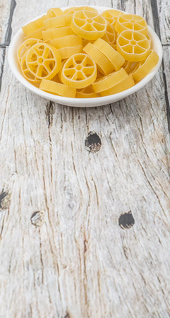 Dried wagon wheel shape pasta or rotelle pasta in white bowl over wooden backgroundの写真素材