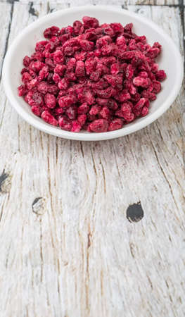 Dried pomegranate seeds in white bowl over wooden background