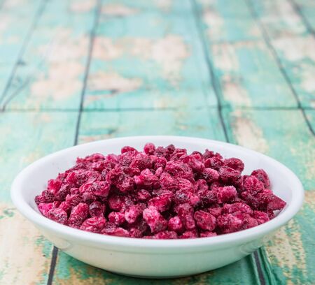 Dried pomegranate seeds in white bowl over wooden background