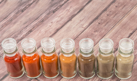 Hot and spicy spices powder, cayenne powder, chilly powder, peppercorn powder, paprika powder, black pepper and white pepper powder in glass vial over wooden backgroundの写真素材