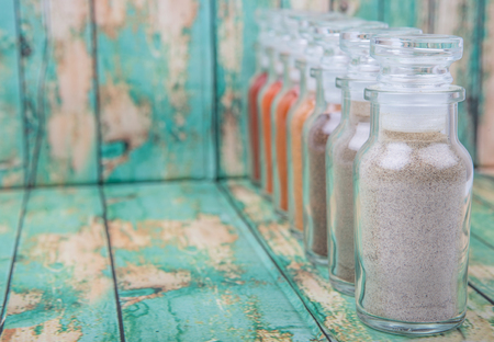 Hot and spicy spices powder, cayenne powder, chilly powder, peppercorn powder, paprika powder, black pepper and white pepper powder in glass vial over wooden backgroundの写真素材