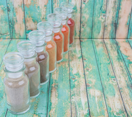 Hot and spicy spices powder, cayenne powder, chilly powder, peppercorn powder, paprika powder, black pepper and white pepper powder in glass vial over wooden backgroundの写真素材