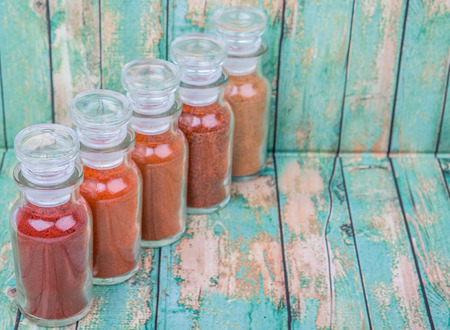 Different type and colors of chilly powder, paprika powder, cayenne powder in glass vial over wooden...
