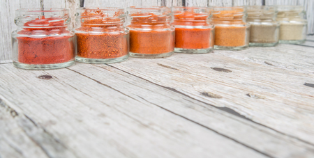 Hot and spicy spices powder, cayenne powder, chilly powder, peppercorn powder, paprika powder, black pepper and white pepper powder in small mason jar over wooden backgroundの写真素材