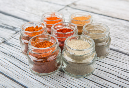 Hot and spicy spices powder, cayenne powder, chilly powder, peppercorn powder, paprika powder, black pepper and white pepper powder in small mason jar over wooden backgroundの写真素材