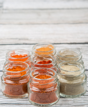 Hot and spicy spices powder, cayenne powder, chilly powder, peppercorn powder, paprika powder, black pepper and white pepper powder in small mason jar over wooden backgroundの写真素材