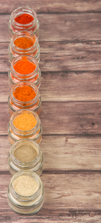 Hot and spicy spices powder, cayenne powder, chilly powder, peppercorn powder, paprika powder, black pepper and white pepper powder in small mason jar over wooden backgroundの写真素材
