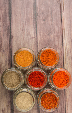 Hot and spicy spices powder, cayenne powder, chilly powder, peppercorn powder, paprika powder, black pepper and white pepper powder in small mason jar over wooden backgroundの写真素材