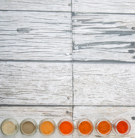Hot and spicy spices powder, cayenne powder, chilly powder, peppercorn powder, paprika powder, black pepper and white pepper powder in small mason jar over wooden backgroundの写真素材