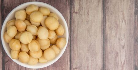 Peeled macadamia nut in white bowl over wooden background