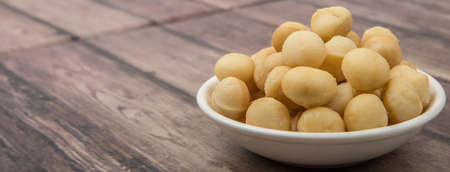 Peeled macadamia nut in white bowl over wooden backgroundの写真素材