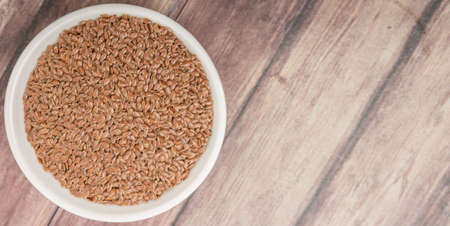 Flax seeds in white bowl over wooden backgroundの写真素材