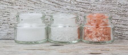 Table salt, sea salt and himalayan salt in mason jar over wooden background