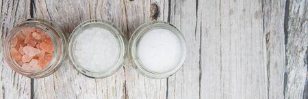 Table salt, sea salt and himalayan salt in mason jar over wooden background