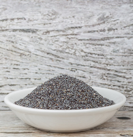 Black poppy seeds in white bowl over wooden backgroundの写真素材