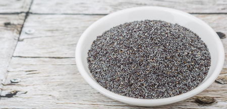 Black poppy seeds in white bowl over wooden backgroundの写真素材