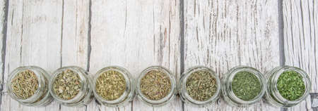 Dried parsley, estragon, marjoram, dill weed, thyme, rosemary and basil herbs in mason jar over wooden backgroundの写真素材