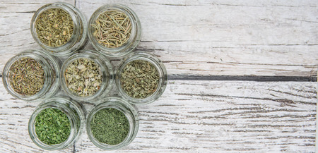 Dried parsley, estragon, marjoram, dill weed, thyme, rosemary and basil herbs in mason jar over wooden backgroundの写真素材