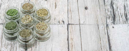 Dried parsley, estragon, marjoram, dill weed, thyme, rosemary and basil herbs in mason jar over wooden backgroundの写真素材