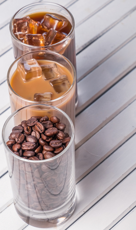Black iced coffee, cold latte, and beans over wooden background