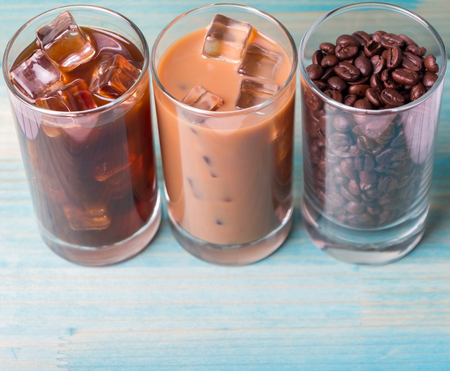 Black iced coffee, cold latte, and beans over wooden background
