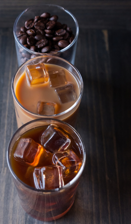 Black iced coffee, cold latte, and beans over wooden background