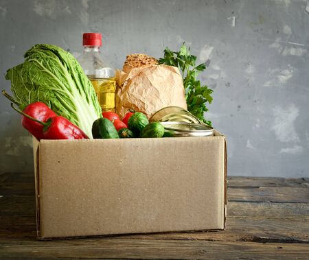 Food in a cardboard box. Food donation or food delivery concept. Light background. Free space for text. Oil, cabbage, salad, vegetables, canned food.の写真素材