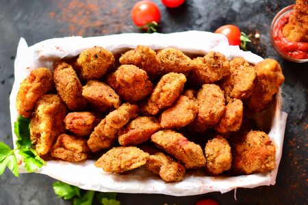 Nuggets in a basket on a dark concrete background. Ketchup, parsley, cherry tomatoes, crispy chicken nuggets.の写真素材