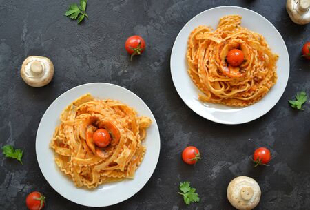 Pasta in a white plate. Pasta with tomato sauce, mushrooms with cherry tomatoes. Dark background. View from above. Free space for text. Delicious foodの写真素材