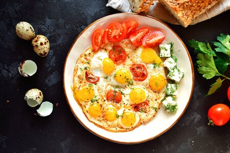 Fried quail eggs in a beautiful plate on a dark table background. Fried eggs with tomatoes and dill. Tasty and healthy breakfast. Top viewの写真素材