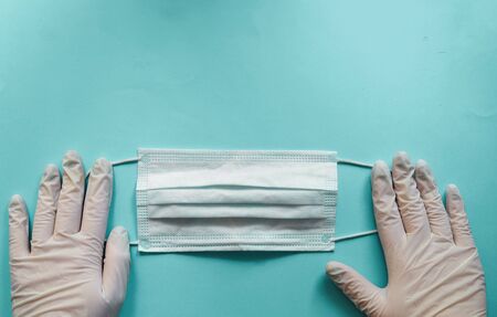 Coronavirus prophylaxis with surgical masks and gloves. Medical mask in the hands. Light blue background. Free space for text.の写真素材