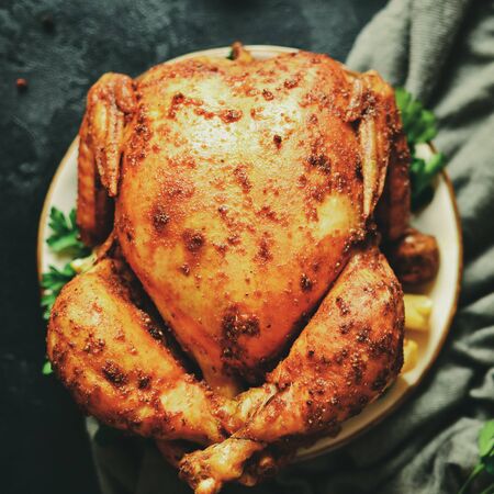 Whole baked chicken with lemon and mushrooms, on a dark background with textile. Curry chicken with a golden crisp.の写真素材