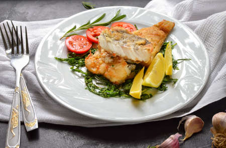 Fried fish fillet with tomatoes, lemon and rosemary. White plate. Dark background. White linen...