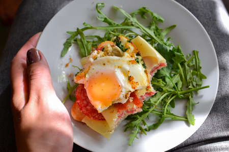 Tasty breakfast. Toast with egg, cheese and sausage. Sandwich in a white plate with arugula. View...