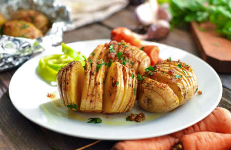 Baked potatoes with carrots. White plate. Wooden background. Delicious and healthy lunch. Hasselback...