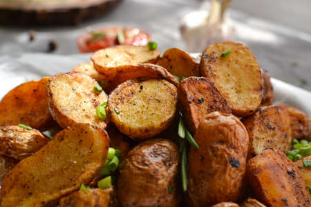 rustic potatoes. Baked potatoes with green onions and herbs on a plate with parchment. Gray background. Close-up.の写真素材