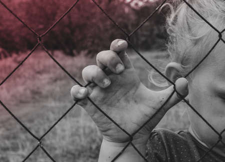 The child holds an iron fence with his hand. Sad child. Cruelty to children.