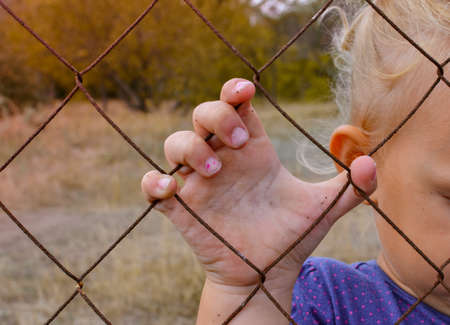 The child holds an iron fence with his hand. Sad child. Cruelty to children.の写真素材