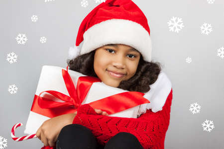 girl with a New Year gift. Joyful girl in a cap of Santa Claus with candyの写真素材